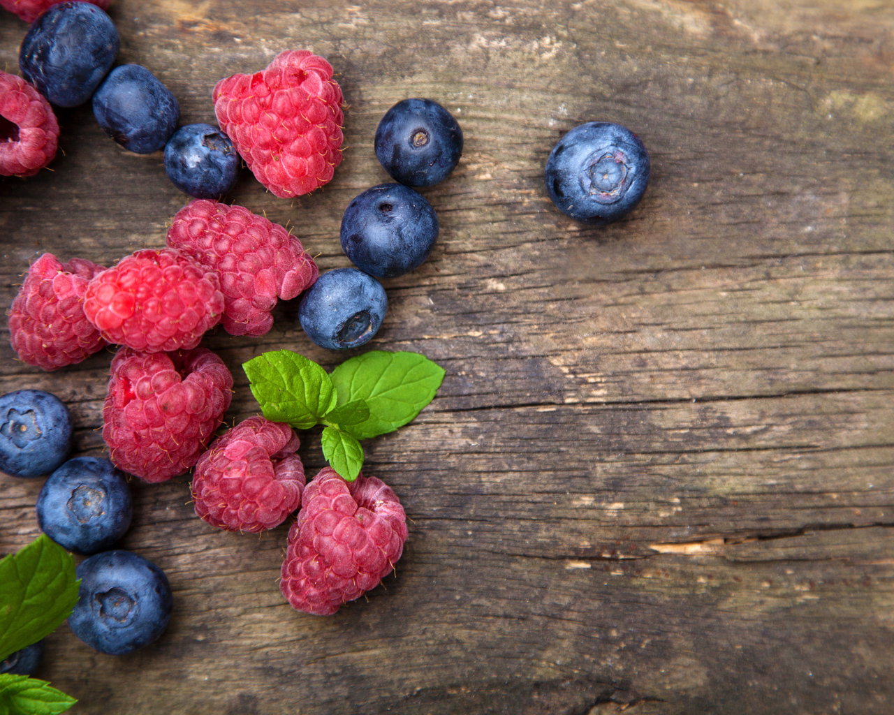 Голубые ягоды черники и красные ягоды малины на деревянном столе