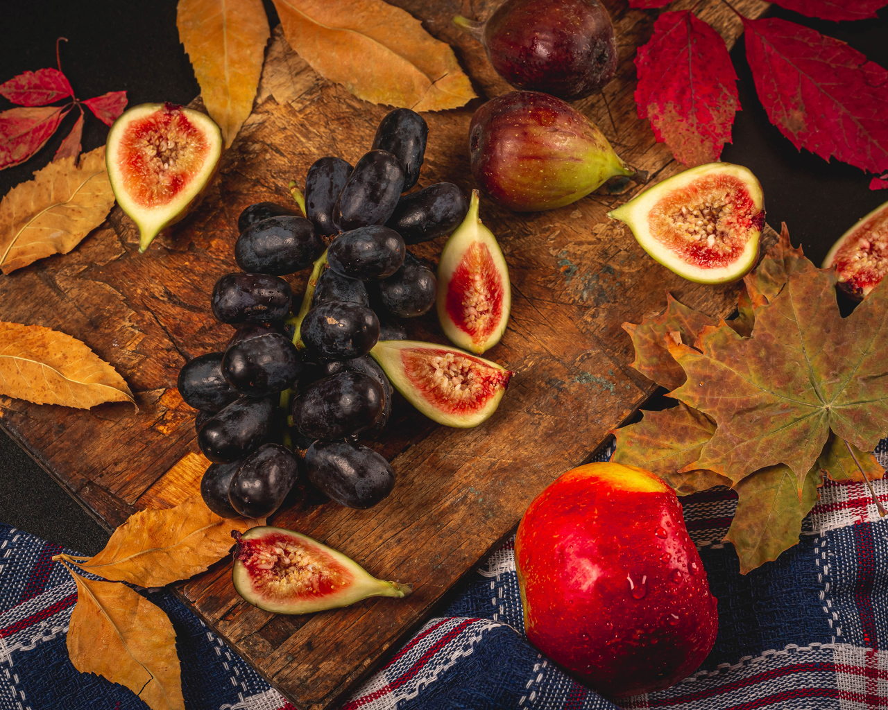 Синий виноград и плоды инжира на столе с листьями