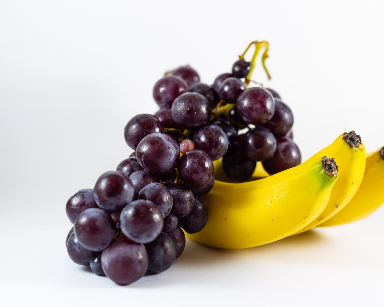 Гроздь розового винограда и бананы на белом фоне