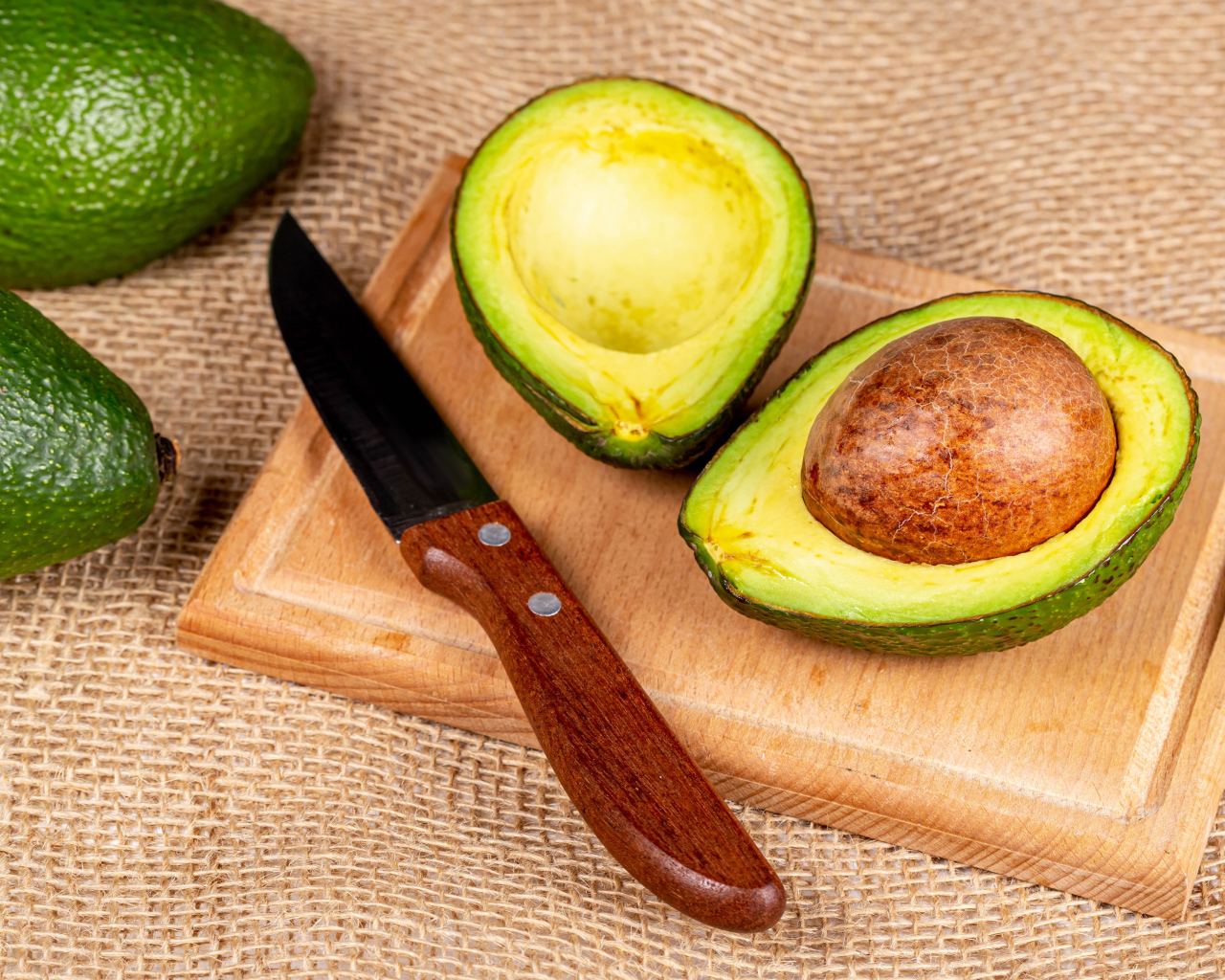 Зеленое авокадо с ножом на разделочной доске