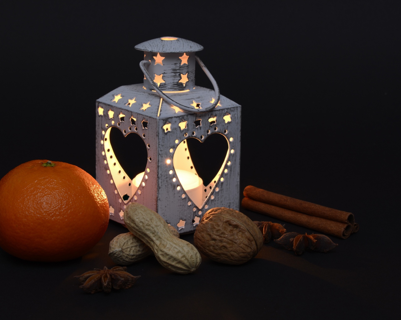 Мандарин, орехи, специи и фонарь на черном фоне