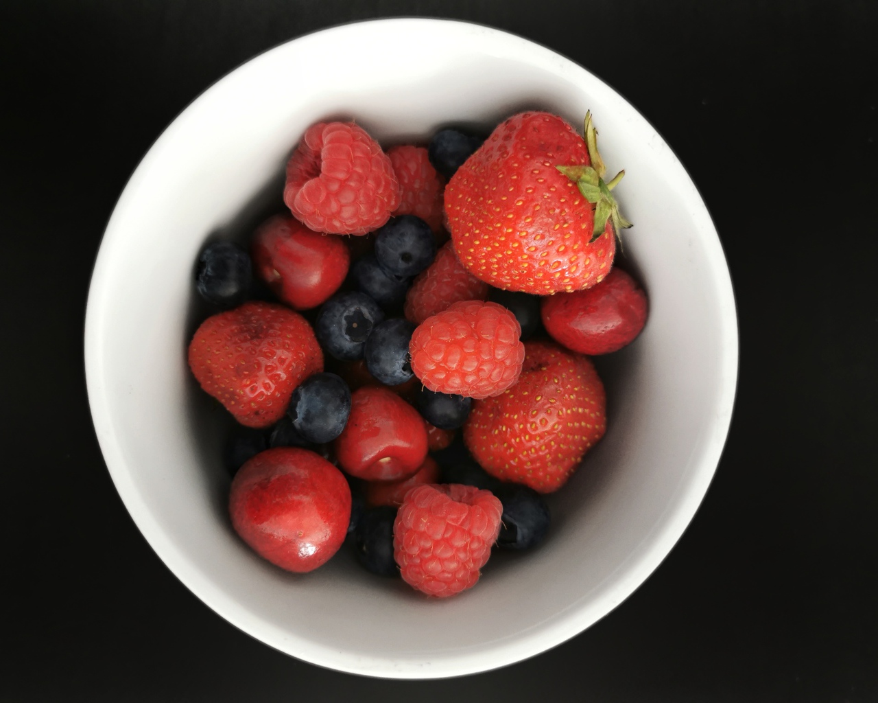 Спелые свежие ягоды в белой тарелке на белом фоне