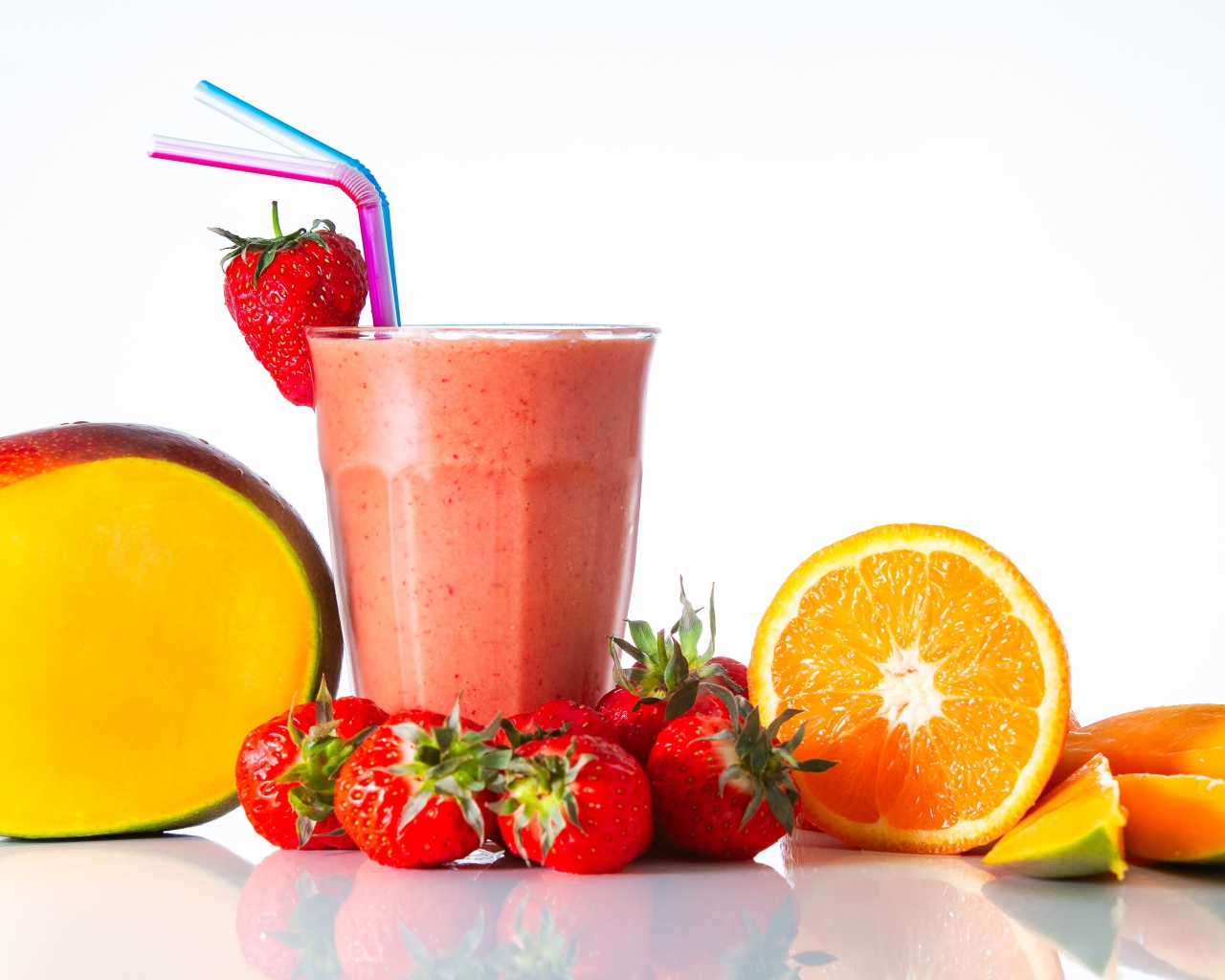 Спелое манго с клубникой и апельсином на столе со смузи