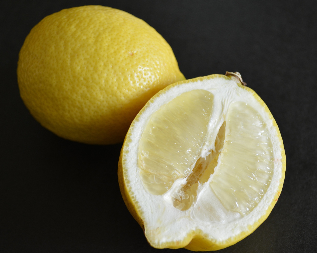 Целый лимон и половина на черной поверхности