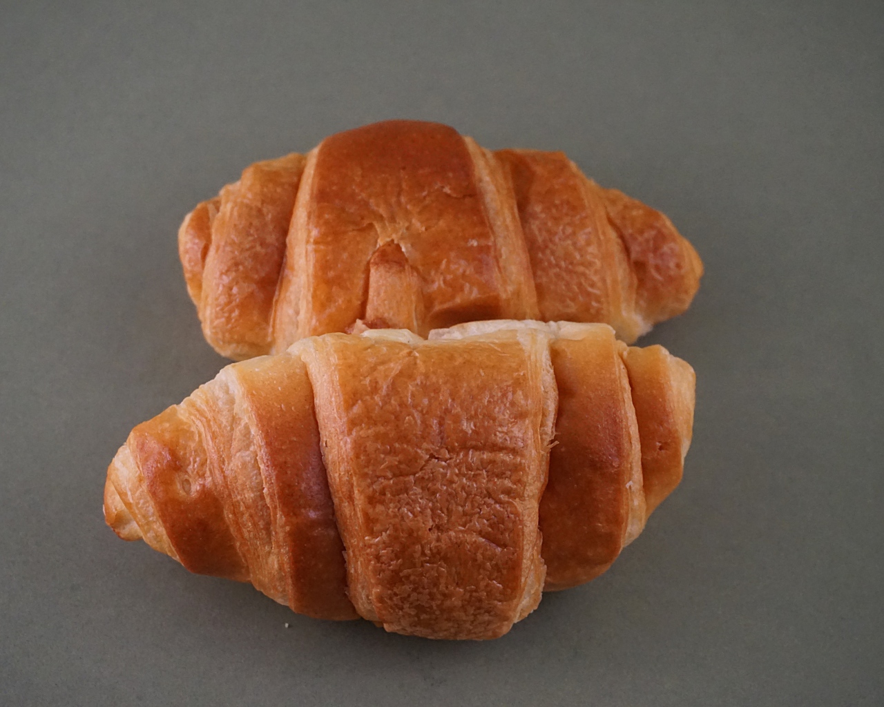 Two fresh croissants on a gray surface