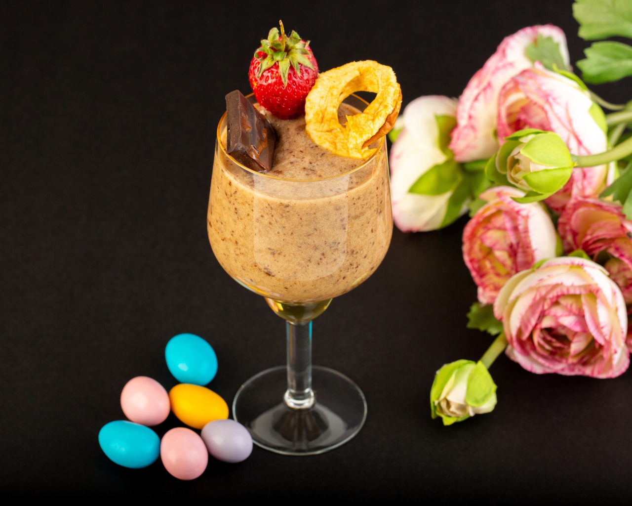 Коктейль с конфетами и букетом лютиков на черном столе