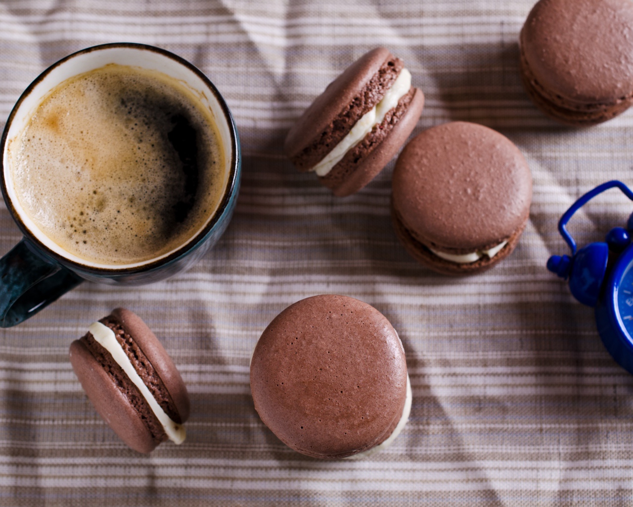 Чашка кофе на столе с десертом макарун и будильником