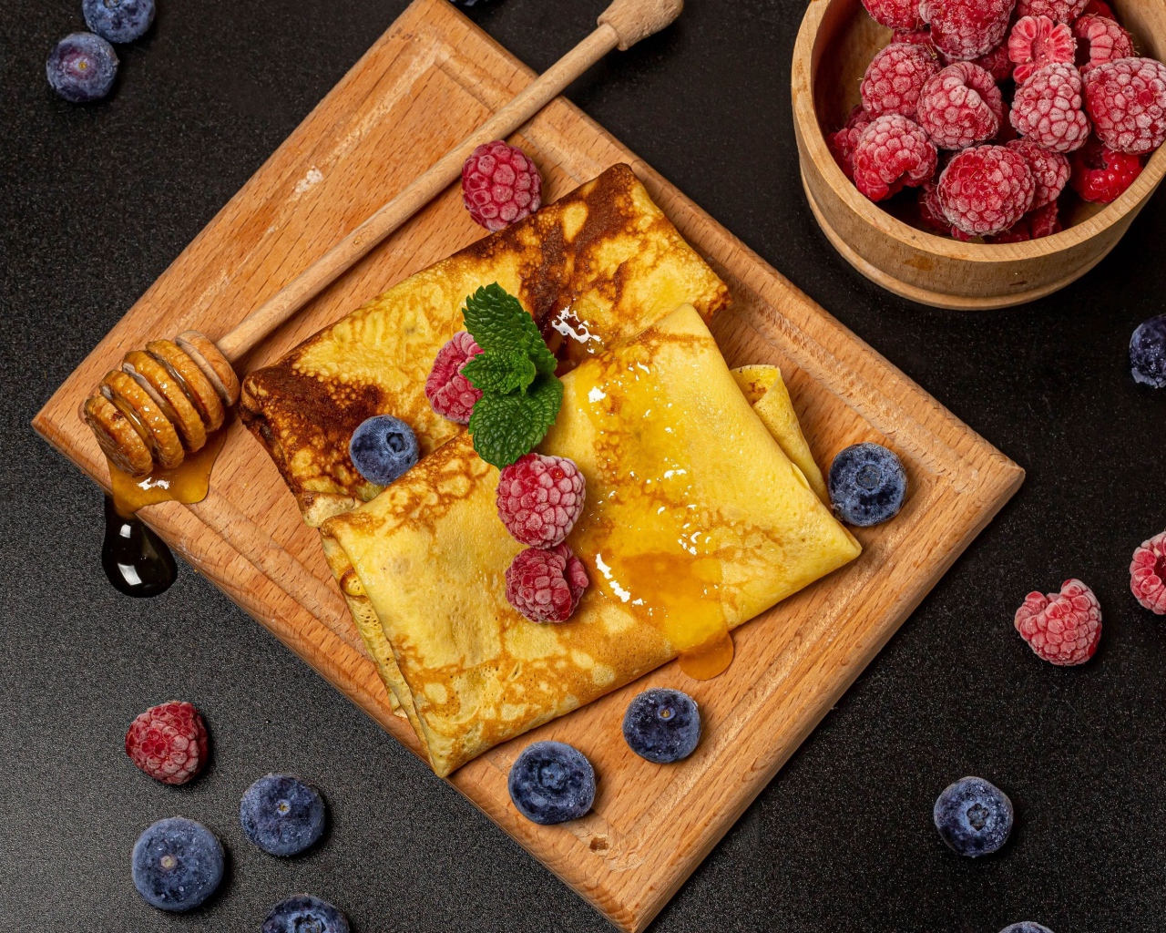 Блины с медом и ягодами черники и малины на черном столе 