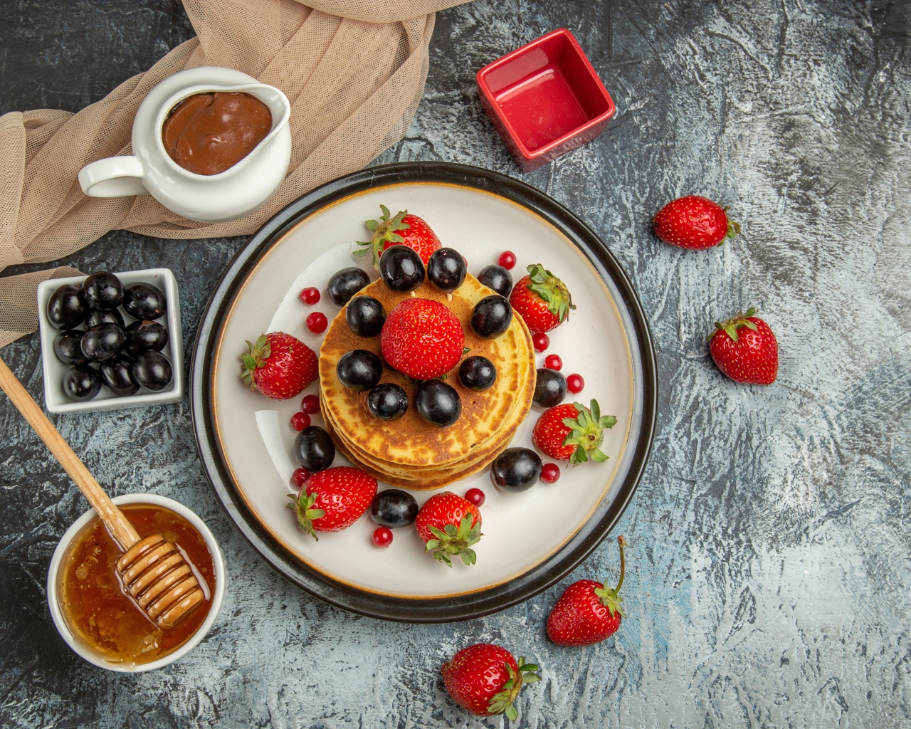 Оладьи с ягодами клубники и винограда на столе с медом