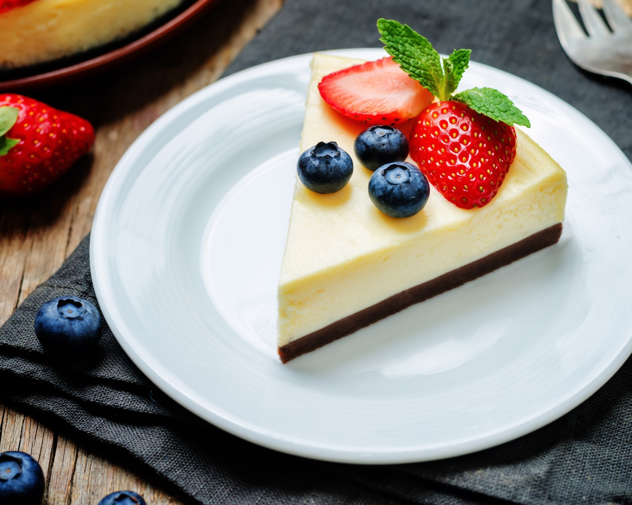 Кусок чизкейка на белой тарелке с клубникой и черникой 