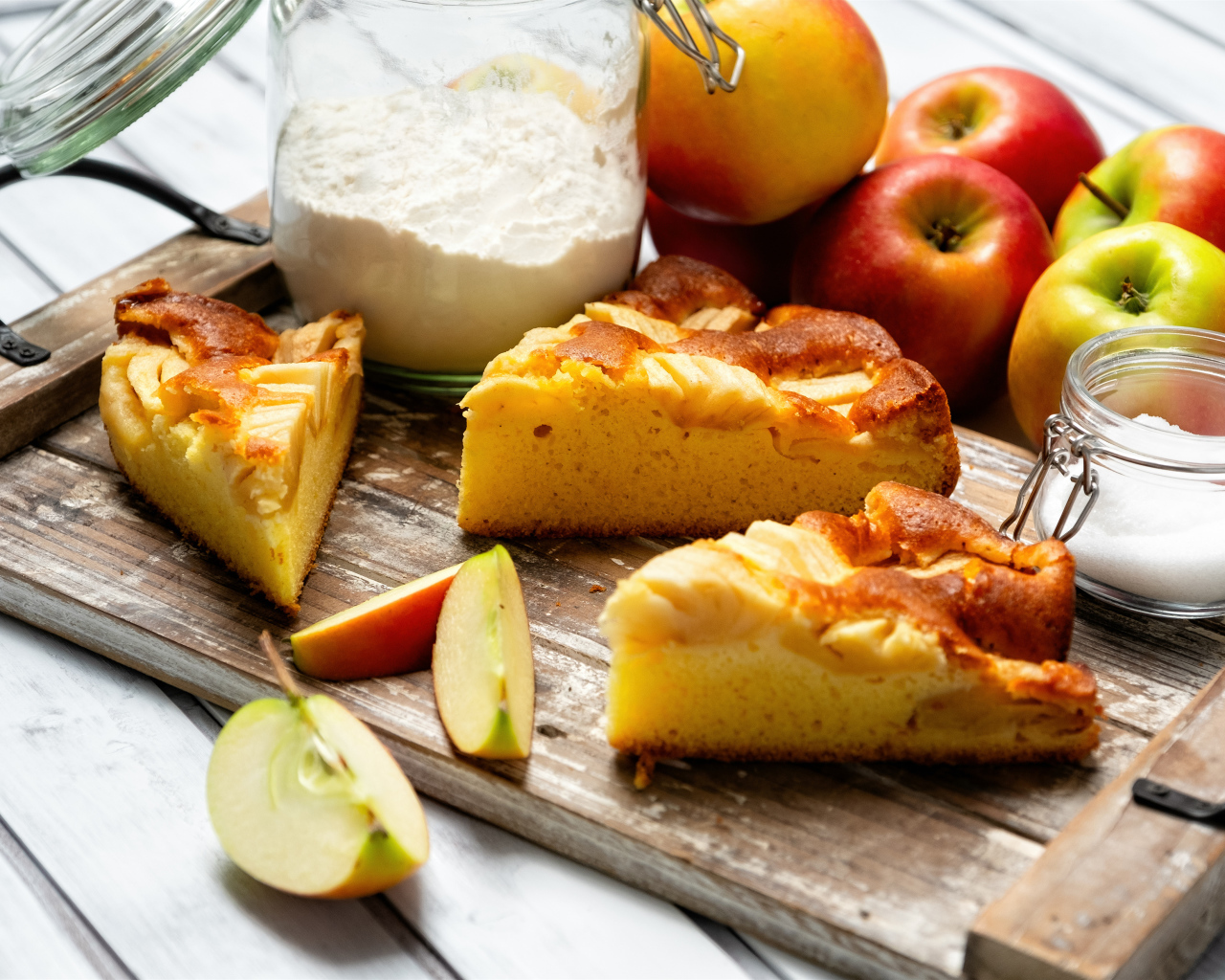 Куски пирога на столе с яблоками и мукой