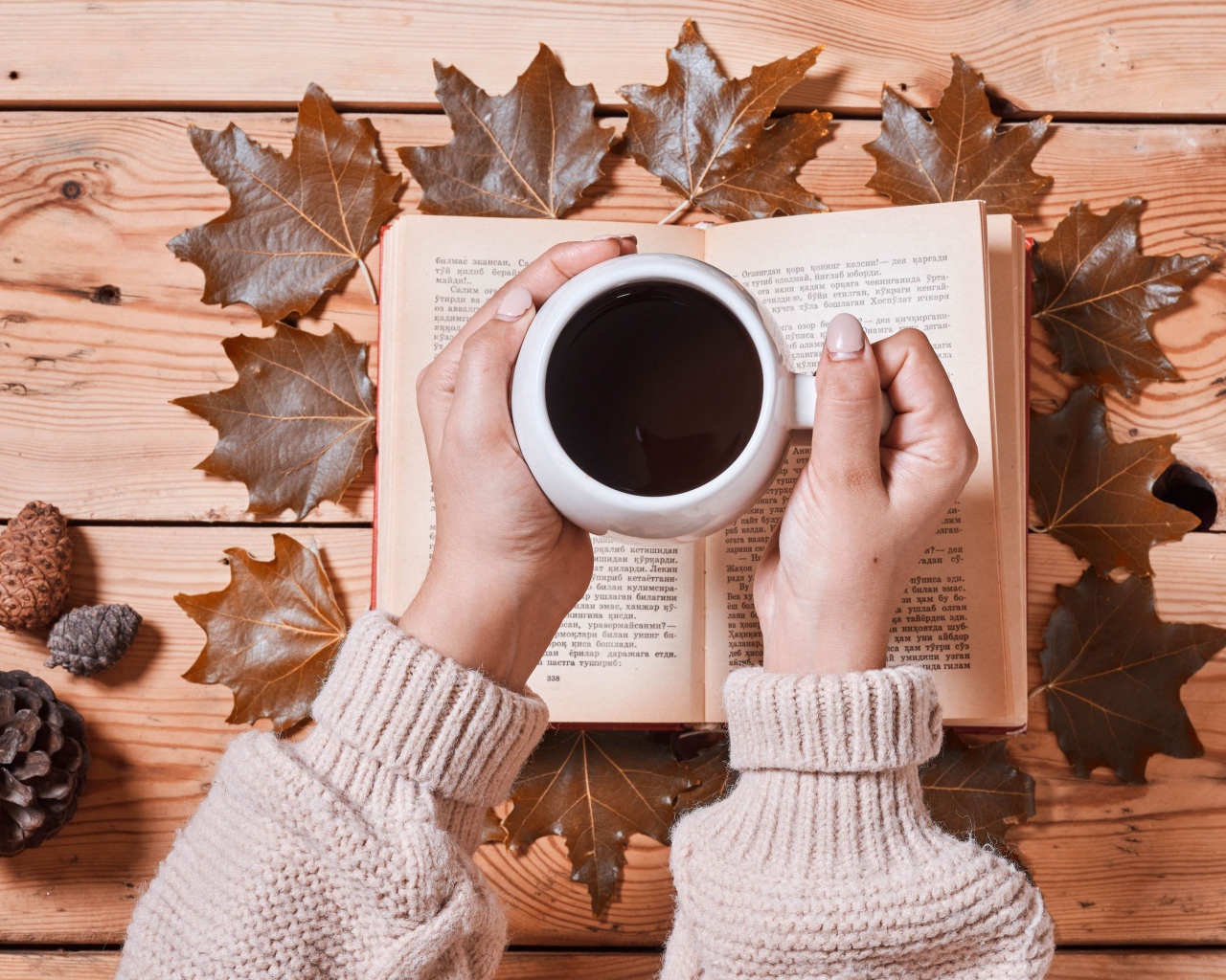 Чашка кофе в руках на столе с книгой и листьями