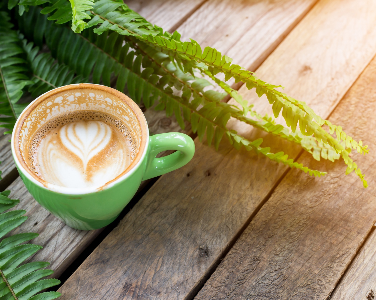 Чашка вкусного капучино  на столе с листьями папоротника