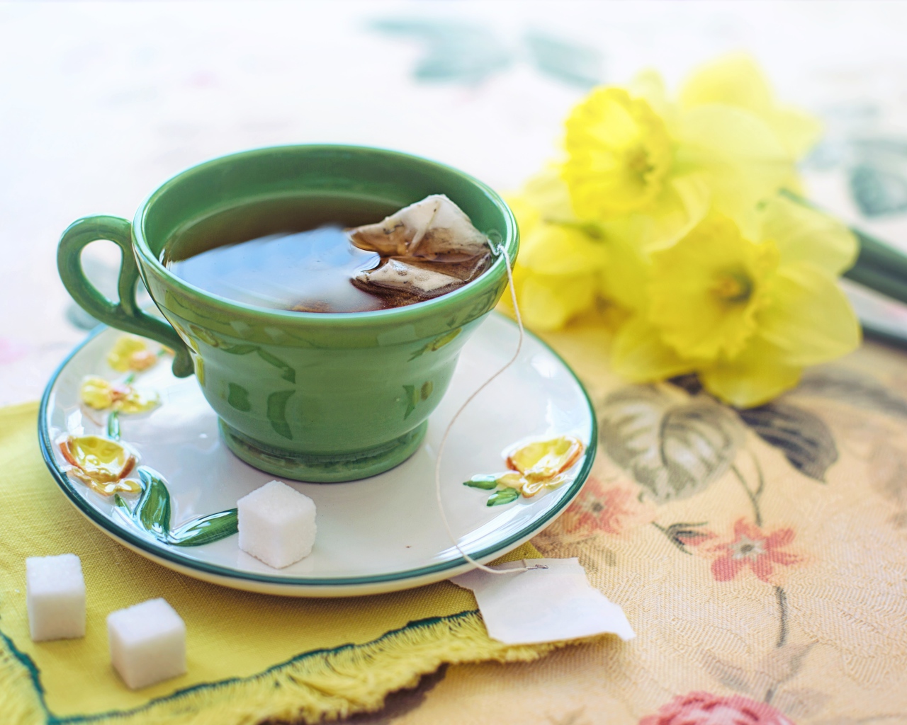 Чашка чая на столе с сахаром и нарциссами