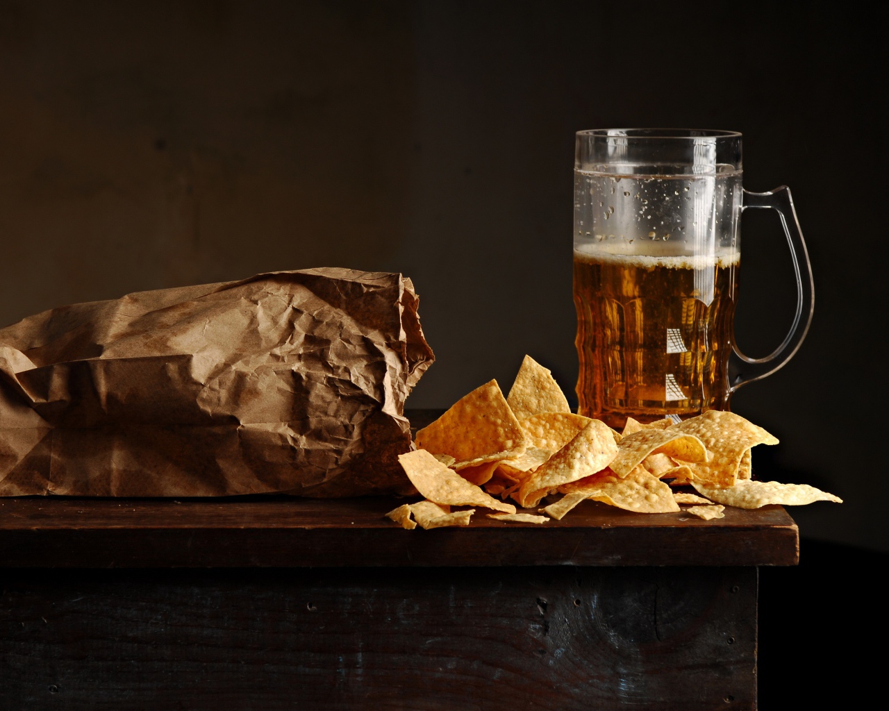 Бокал пива с чипсами в пакете на столе