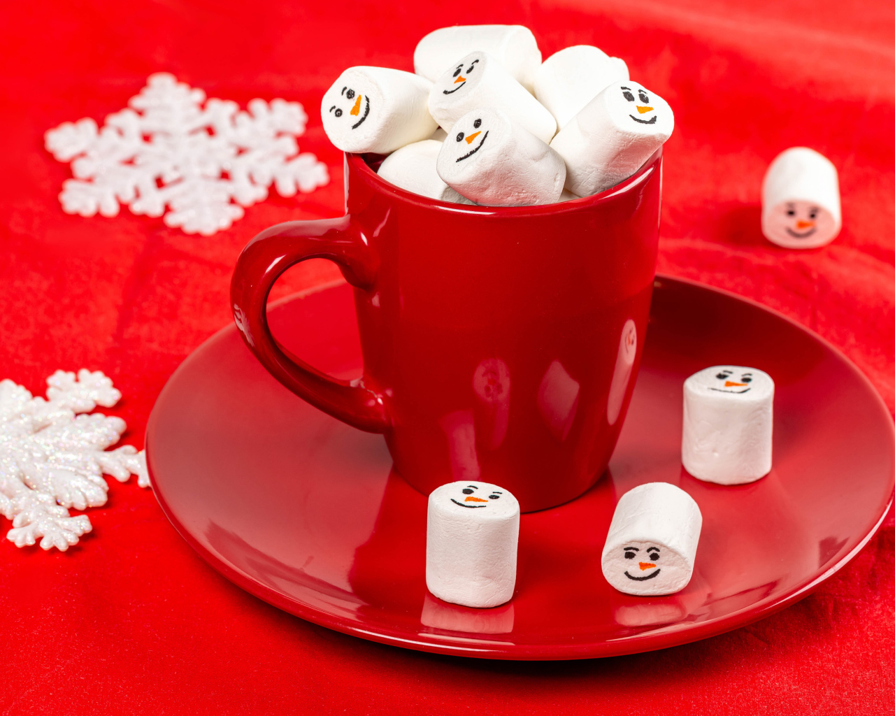 Красная чашка с маршмеллоу на столе со снежинками