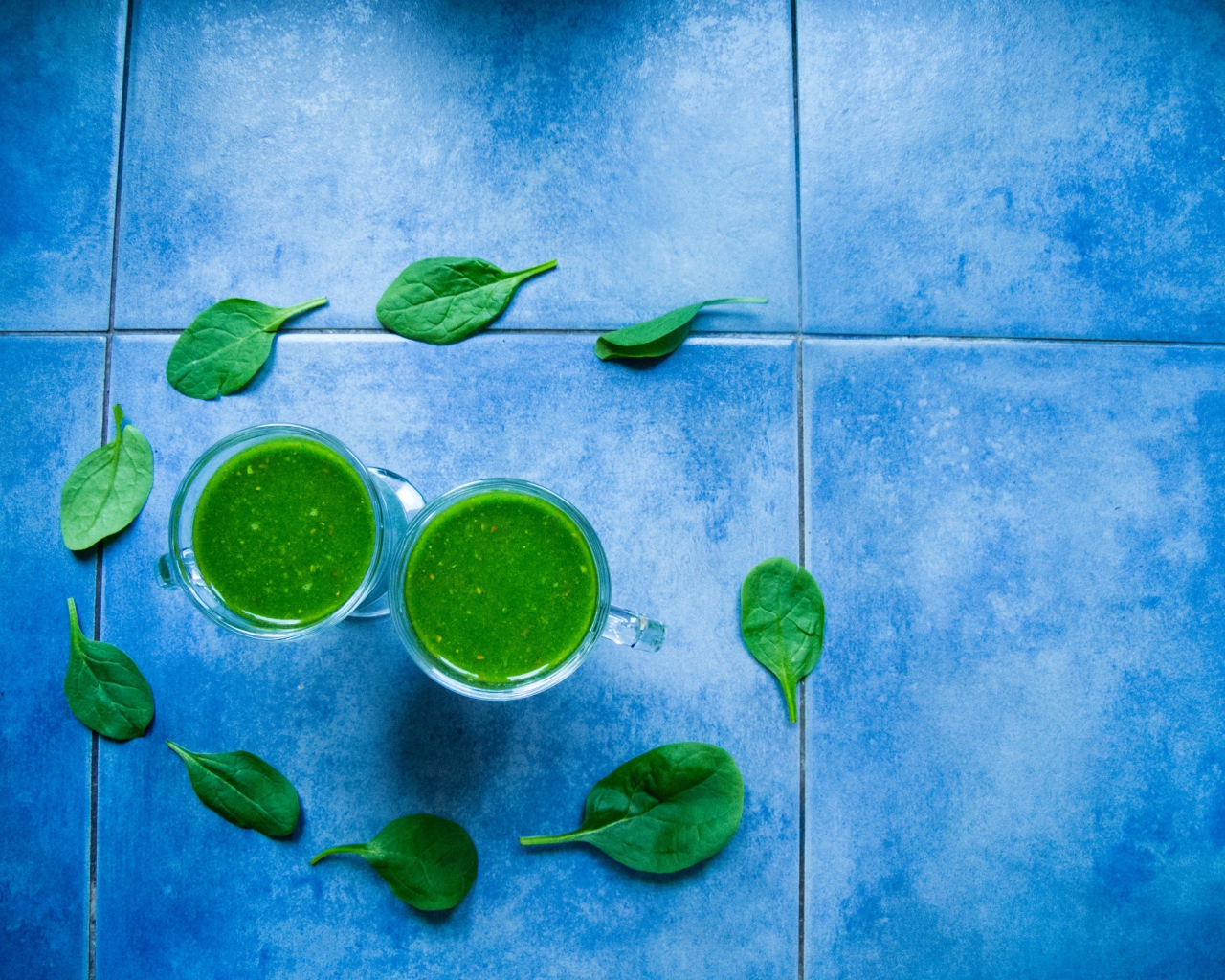 Два зеленых смузи с листьями базилика на голубом фоне