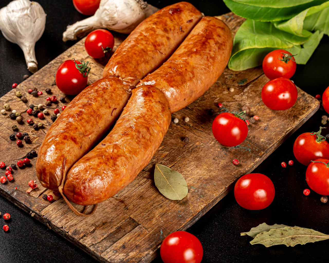 Мясные колбаски на доске с овощами