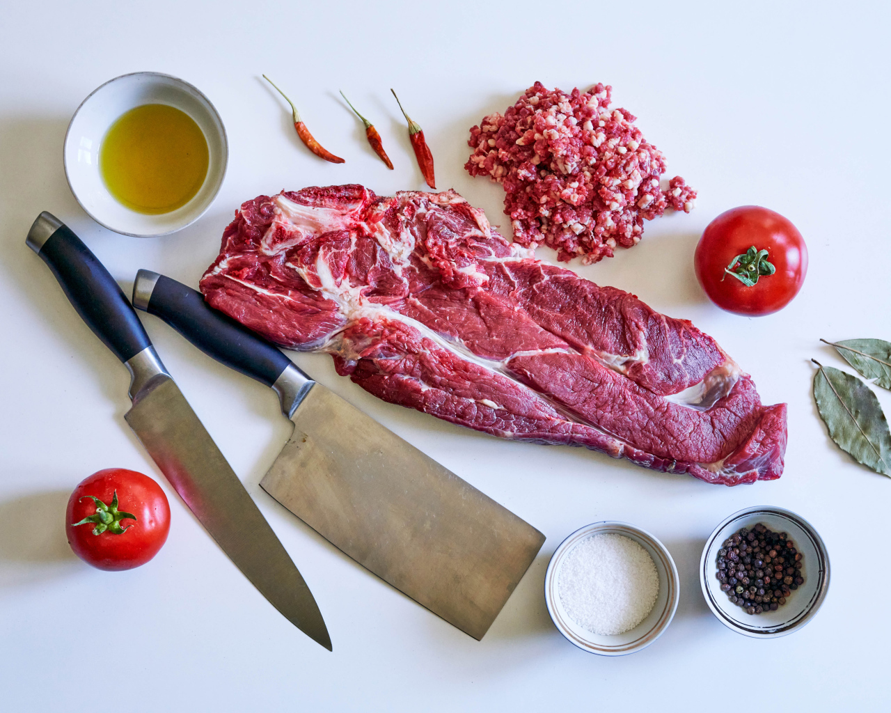 Кусок мяса со специями и ножами на столе 