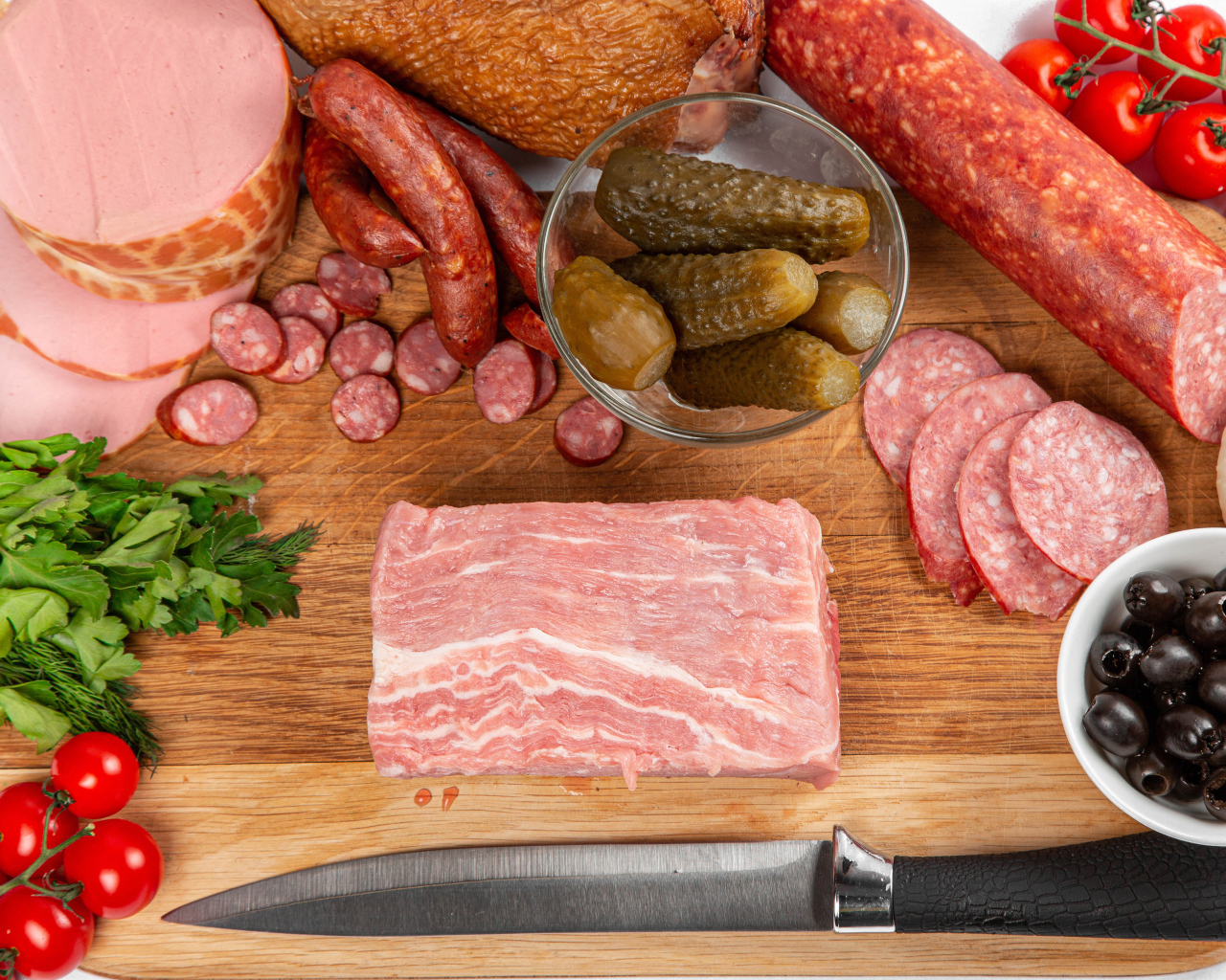 Колбаса на столе с огурцами, помидорами и зеленью 