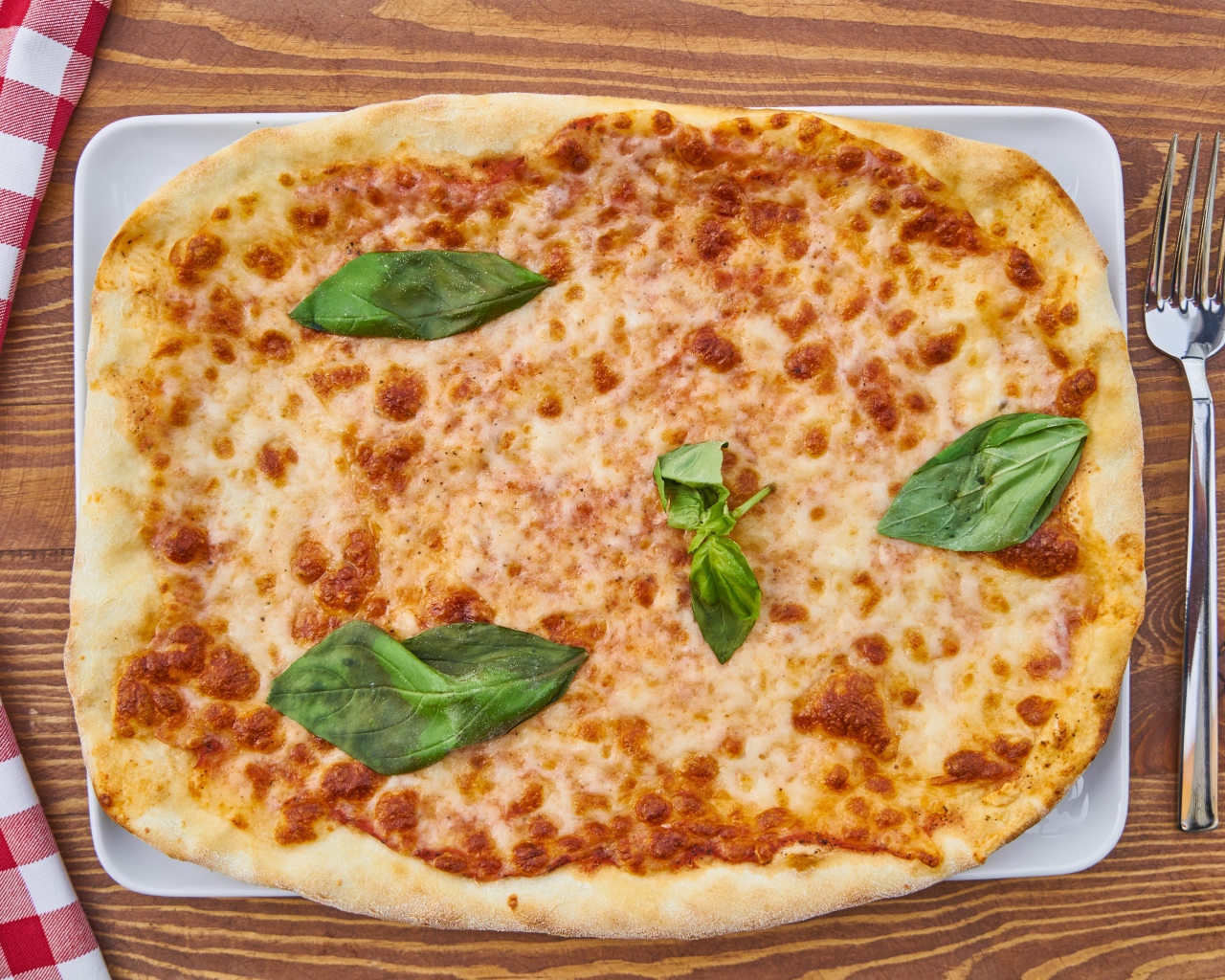 Пицца с сыром и листьями базилика на столе со столовыми приборами