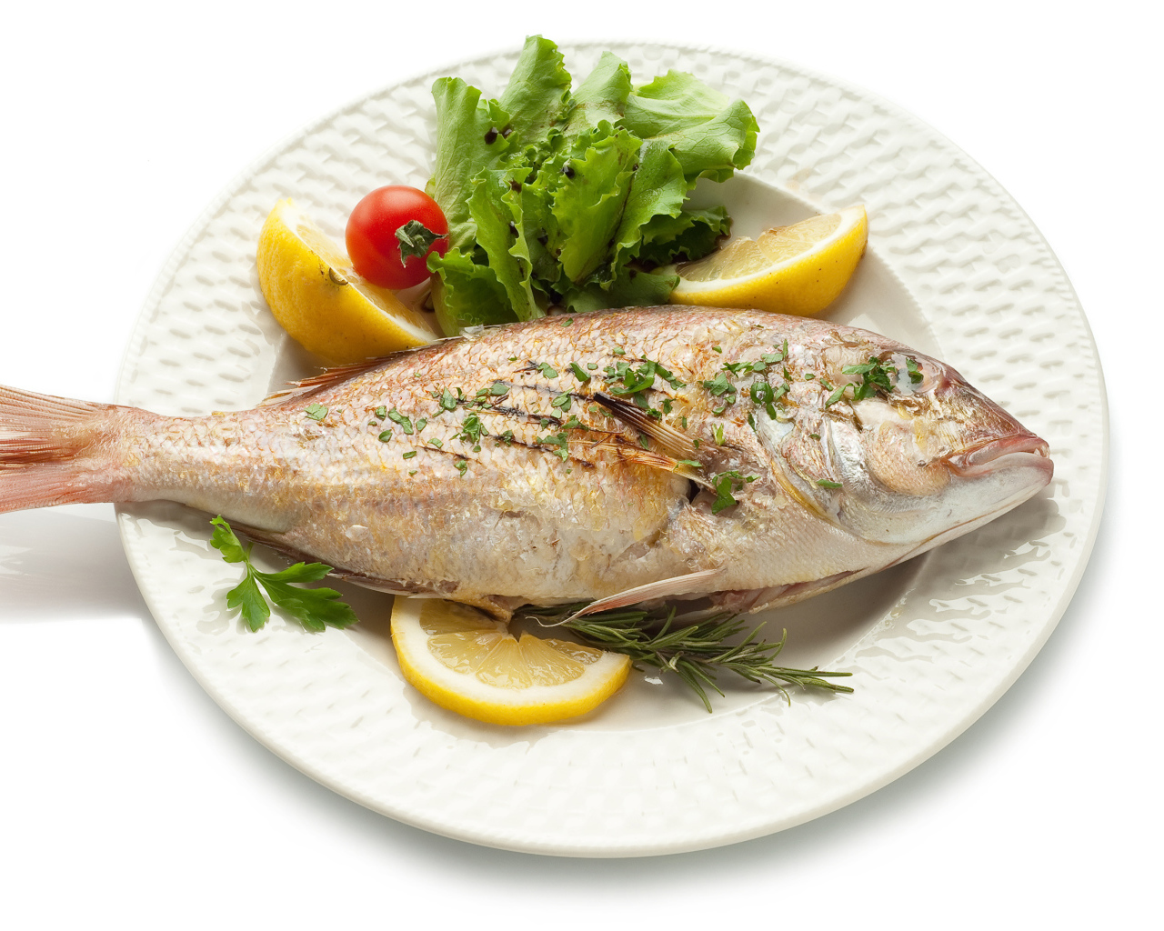 Запеченная рыба на тарелке с зеленью и лимоном