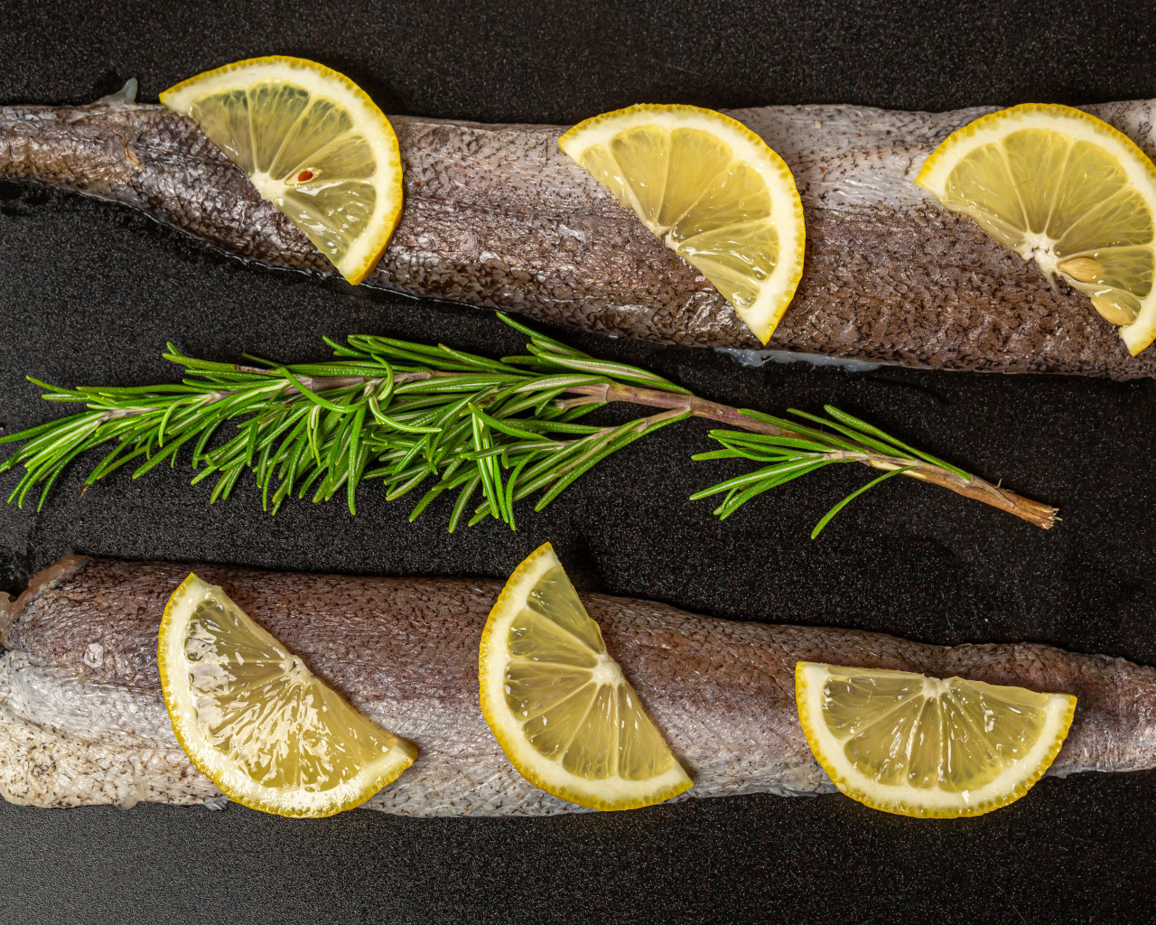 Свежее филе рыбы с лимоном и розмарином на черном фоне