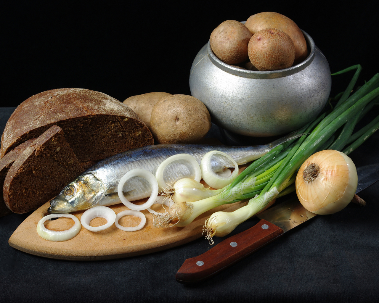 Сельдь на столе с картофелем, черным хлебом и луком 