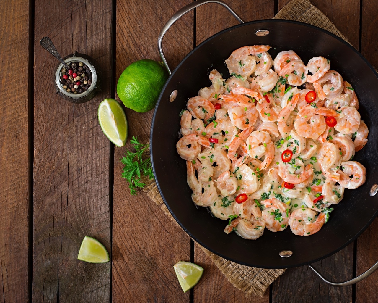 Креветки с соусом в сковороде на столе с лаймом