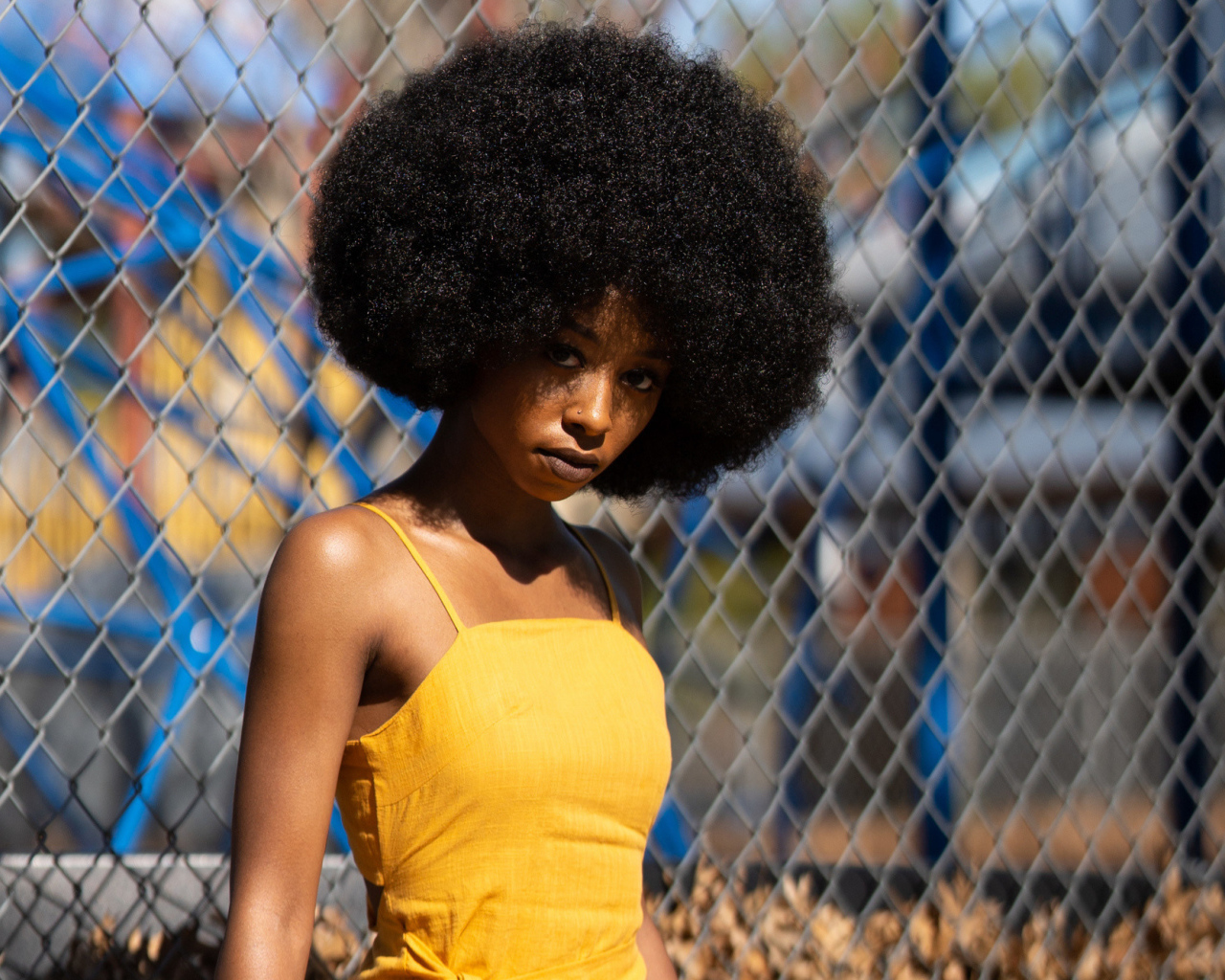 Темнокожая девушка в желтом платье стоит у сетки