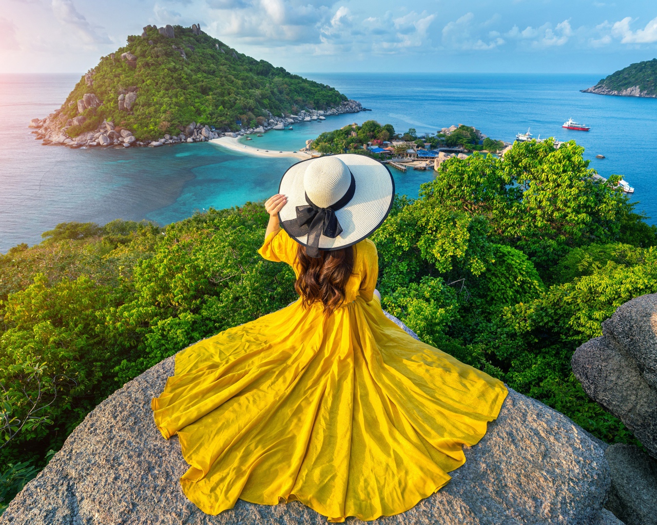 Девушка в красивом желтом платье сидит на камне с видом на море