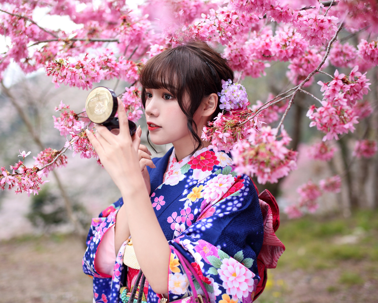 Девушка в кимоно стоит у куста сакуры