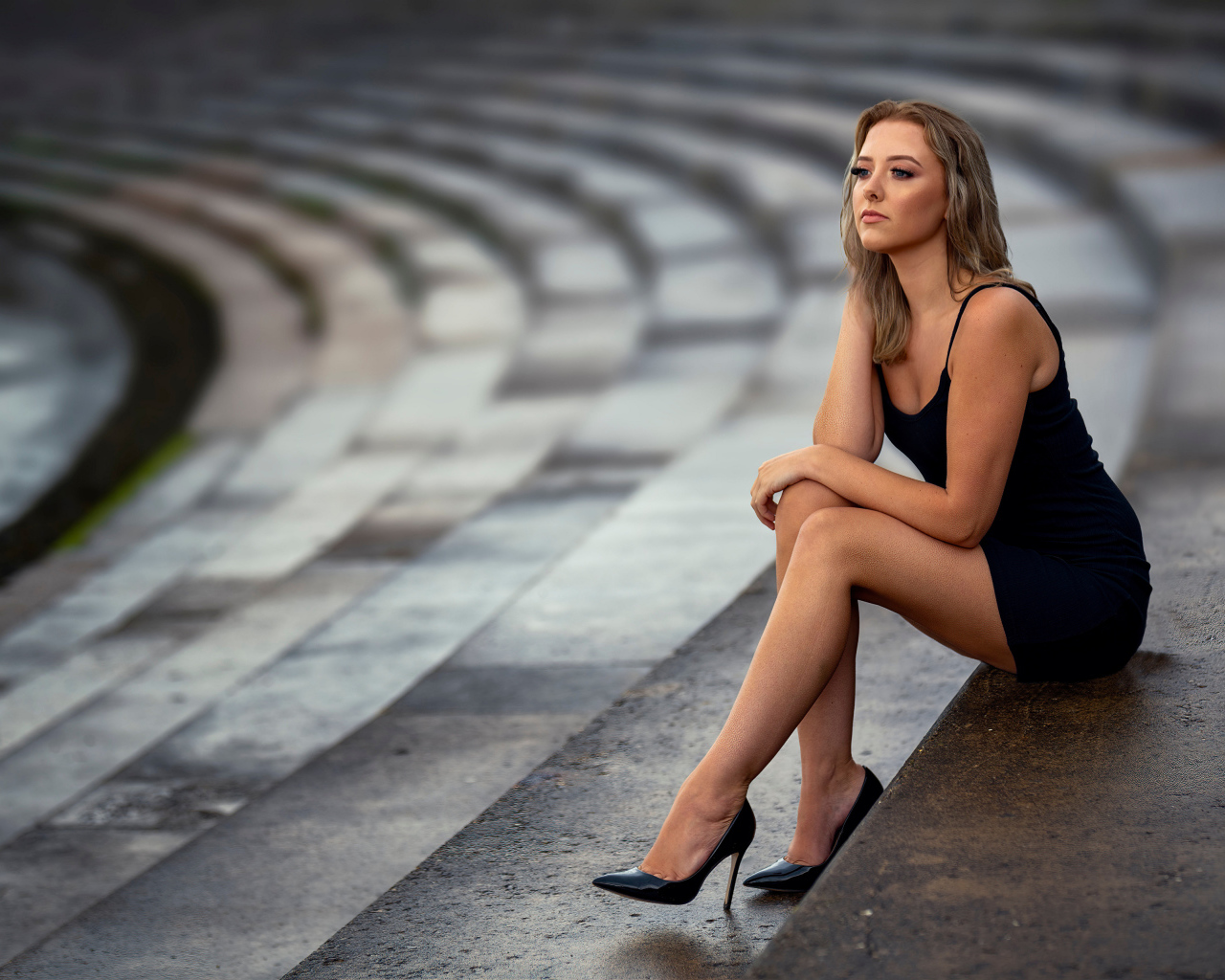 Девушка в коротком черном платье сидит на ступеньках