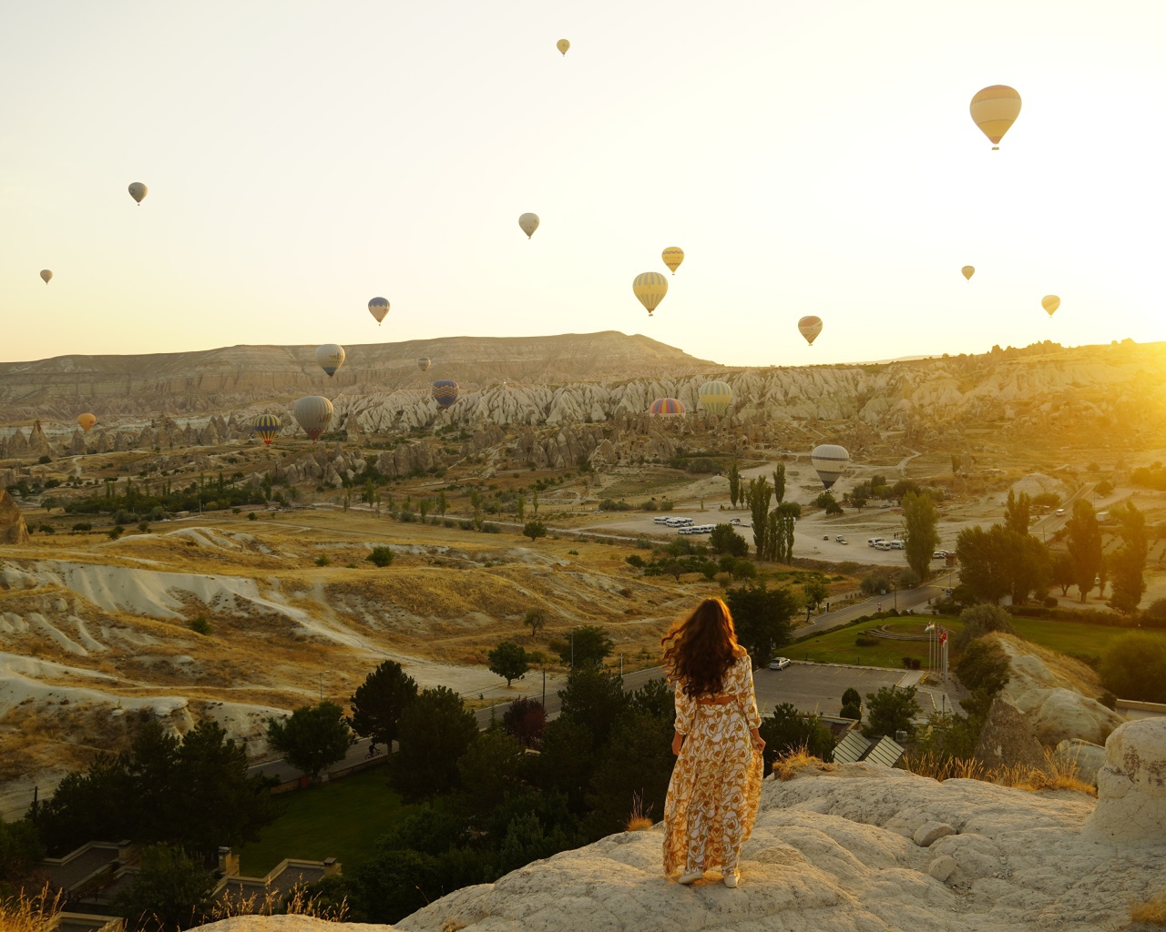 Девушка стоит на краю скалы на фоне неба с воздушными шарами