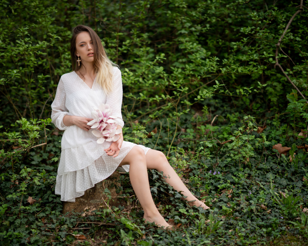 Молодая девушка в белом платье сидит на камне в лесу 