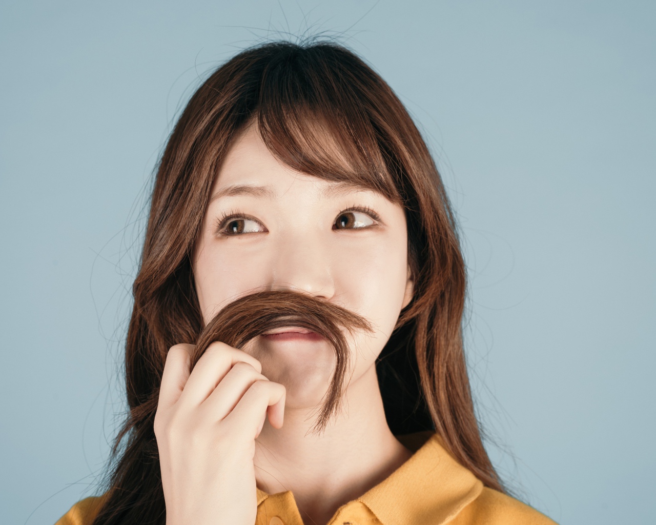 Девушка азиатка закрыла лицо волосами на сером фоне 