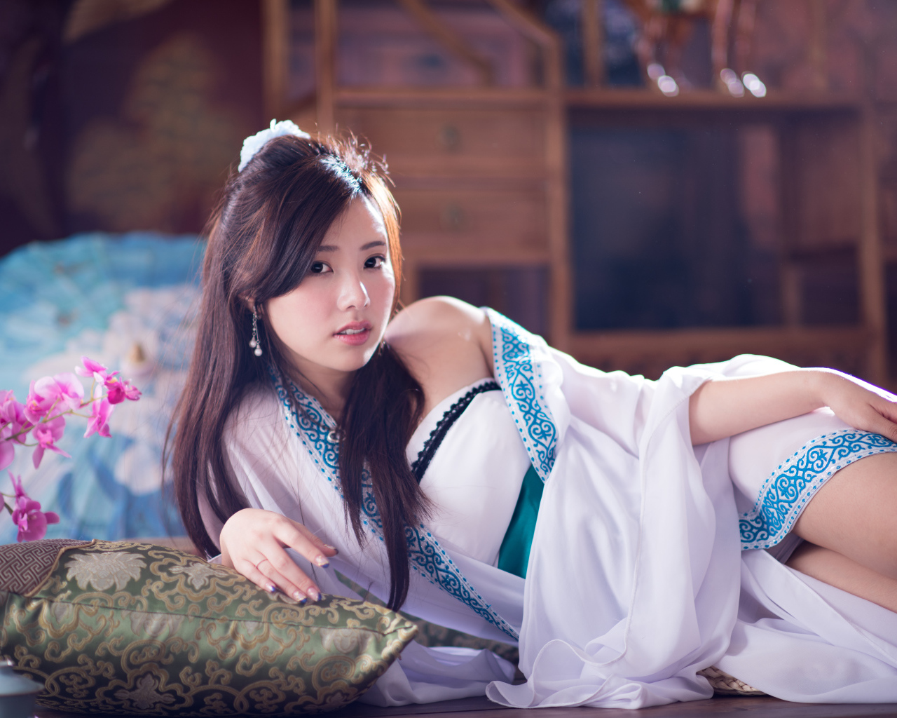 Девушка азиатка в красивом платье лежит на кровати 