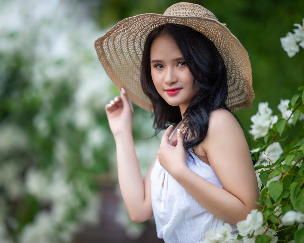 Девушка азиатка в большой шляпе у зеленого куста