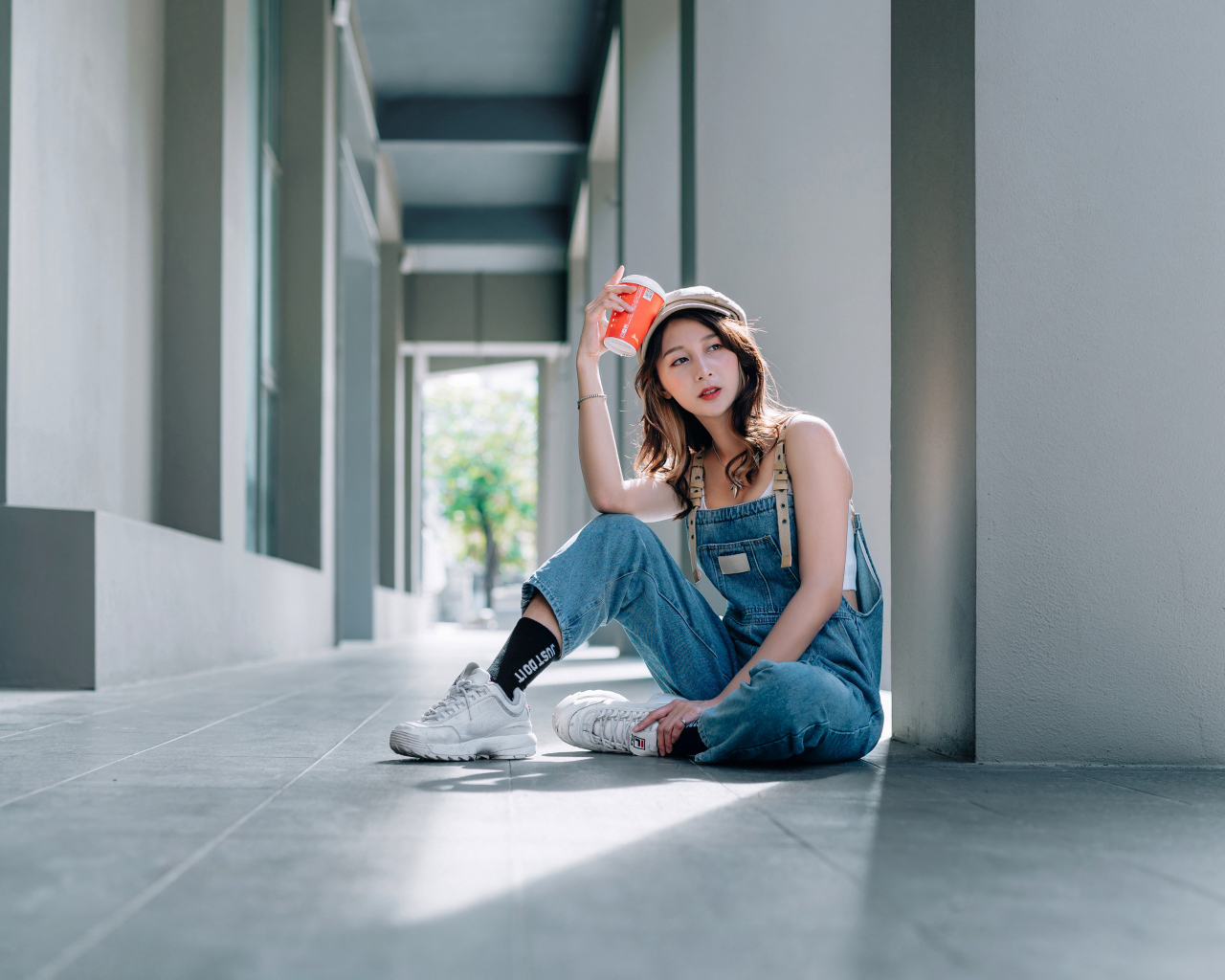 Девушка азиатка в синем комбинезоне с кофе в руке 