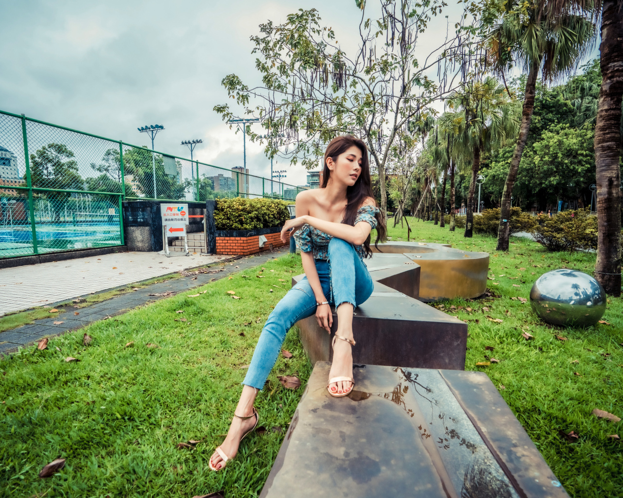 Девушка азиатка в джинсах сидит в парке 