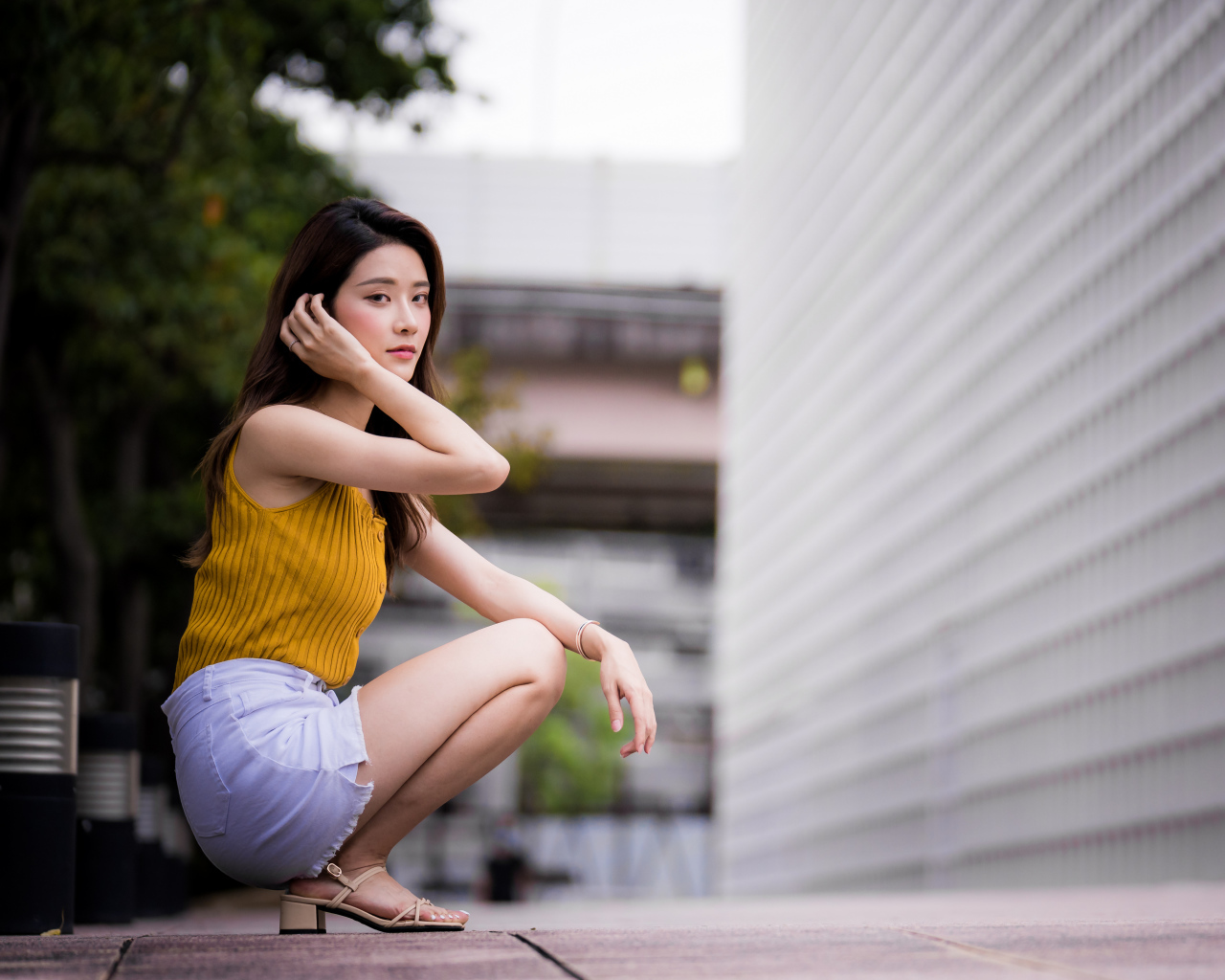 Девушка азиатка сидит на корточках у стены