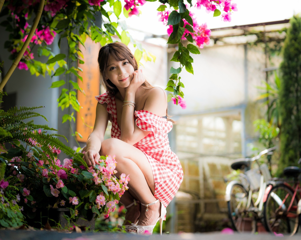 Девушка азиатка сидит на корточках у розового цветка