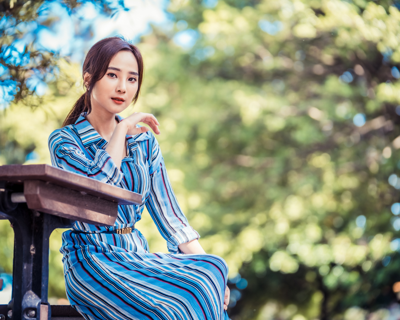 Красивая девушка азиатка в платье  за столом в парке 