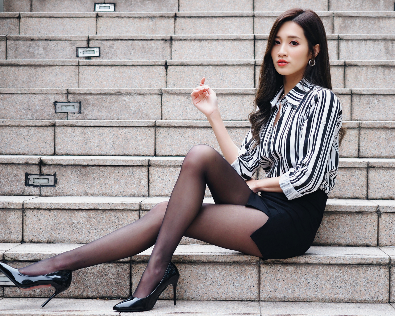 Красивая девушка азиатка в юбке сидит на ступеньках