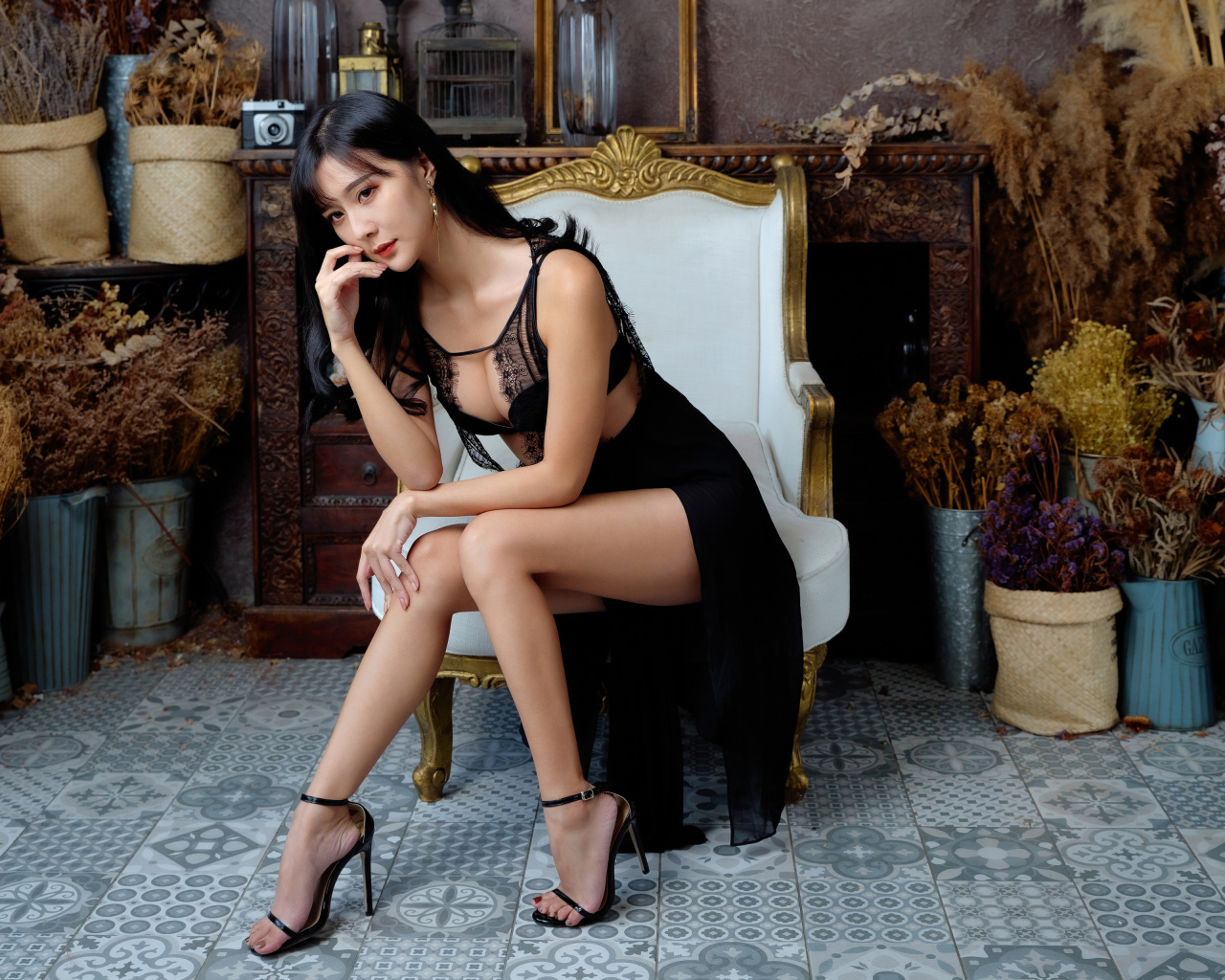 Красивая девушка азиатка в черном платье сидит в белом кресле 