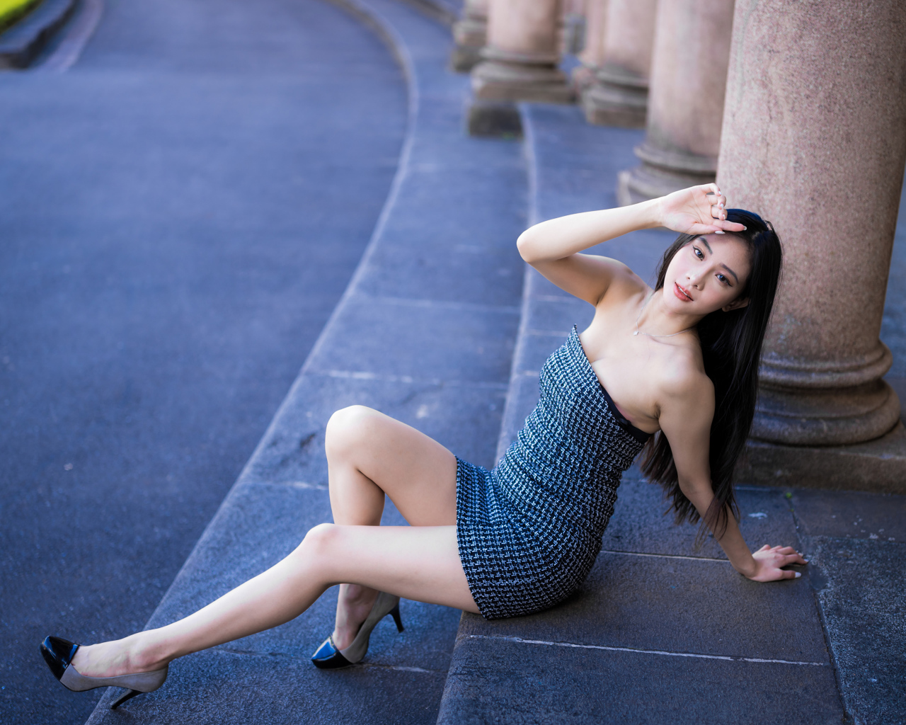 Красивая девушка азиатка в сером платье сидит на ступеньках