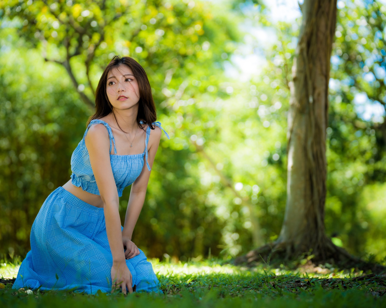 Красивая азиатка в голубом платье сидит на траве в парке 