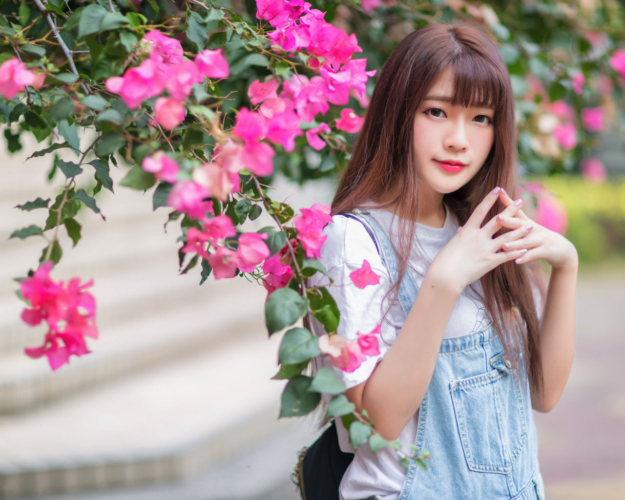 Красивая милая азиатка стоит у куста с розовыми цветами