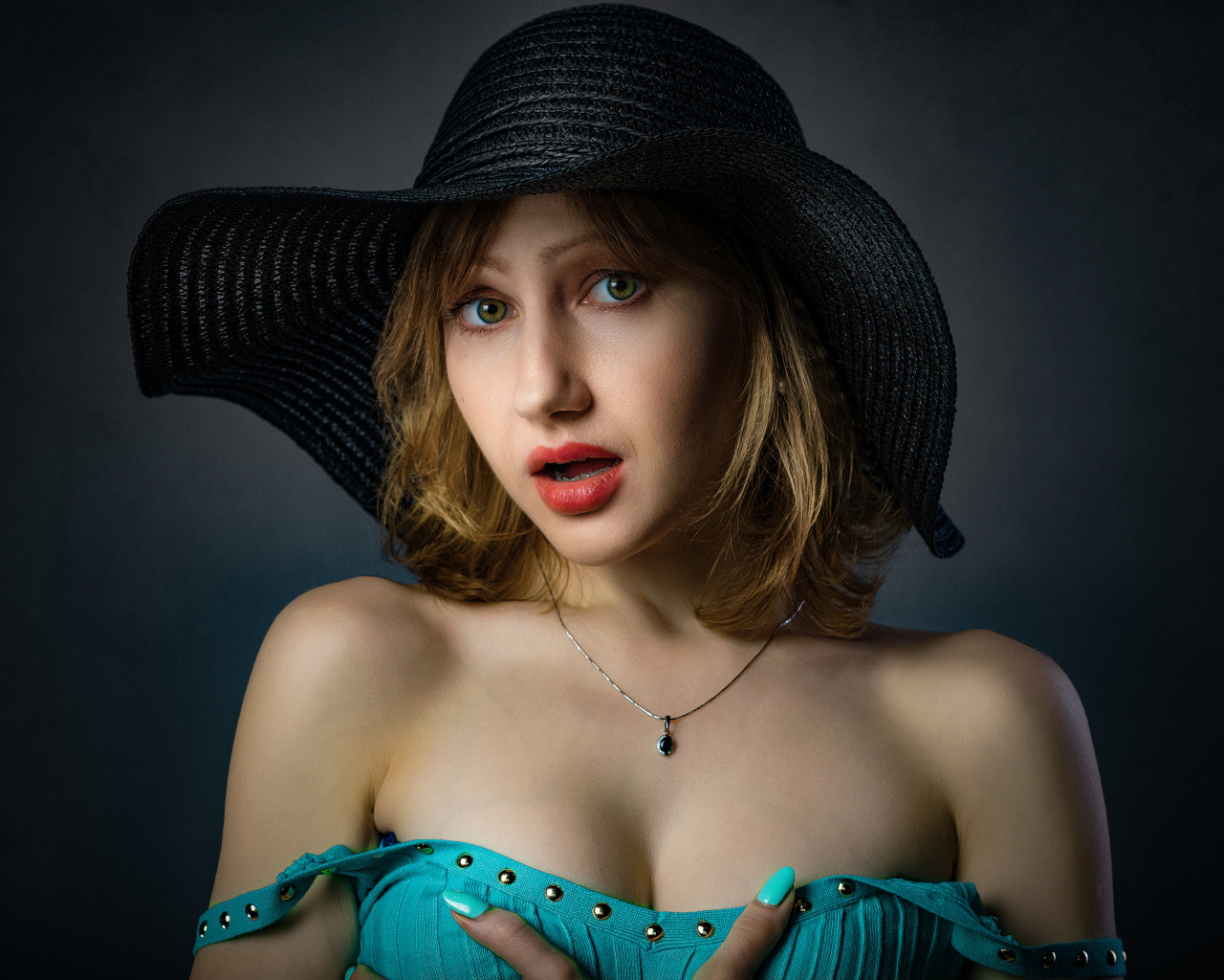 Красивая девушка в большой черной шляпе на сером фоне 