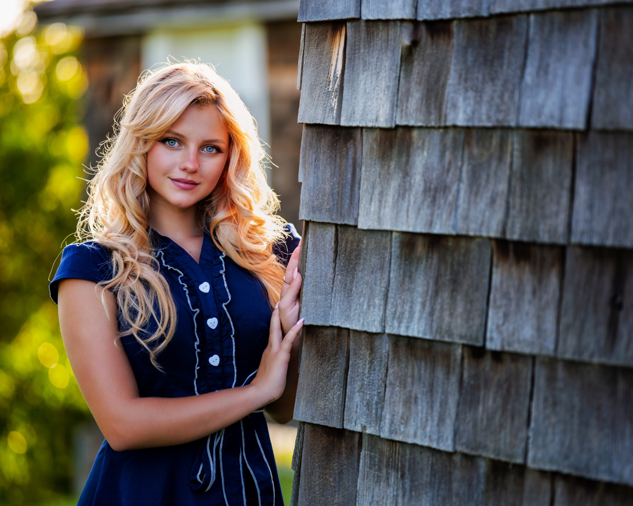 Голубоглазая блондинка в платье стоит у стены 